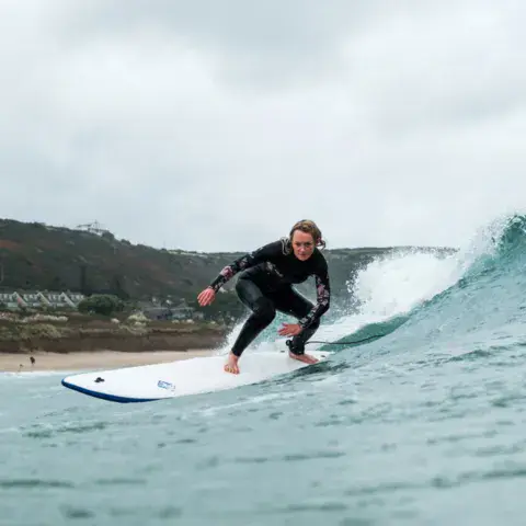 Surfeur sur une vague, avec une plage et des collines derrière