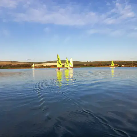 Dériveurs jaunes sur un lac au soleil couchant
