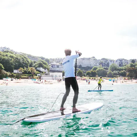 Moniteur de paddle sur l'eau, avec la plage et la ville en arrière-plan