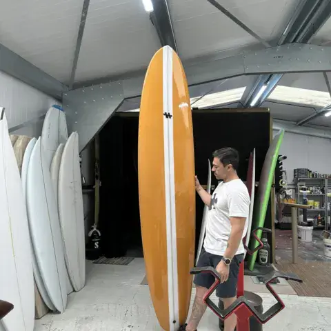 Le shaper à côté d'une planche, dans l'atelier