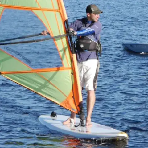 Un élève de windsurf sur sa planche, des voiliers à l'arrière