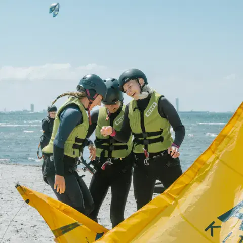 Élèves en gilet et casque autour d'une aile de kite, sur la plage