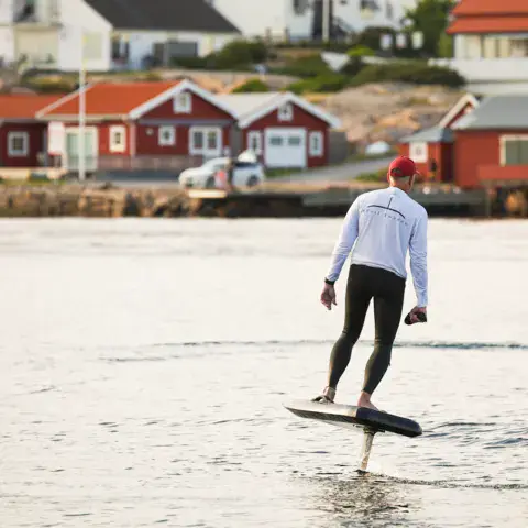 Rider sur un e-foil devant des cabanes rouges en bord de mer