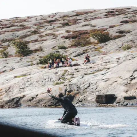 Élève lancé sur un e-foil, avec des spectateurs sur les rochers