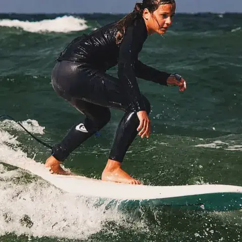 Surfeuse debout sur sa planche dans une vague