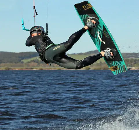 Un kitesurfeur en plein saut sur un lac bordé de collines boisées