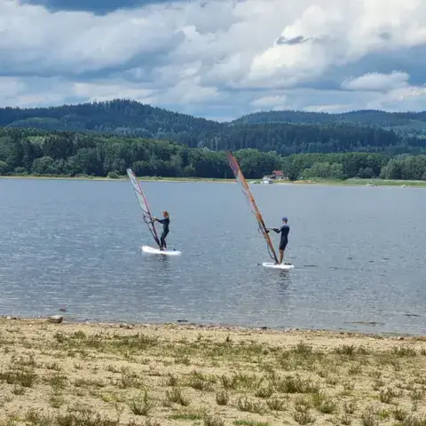Deux véliplanchistes sur le lac, face à une plage de sable