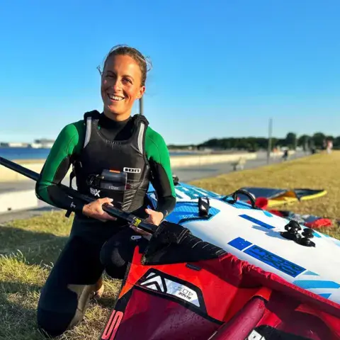 Windsurfeuse en combinaison à côté de son gréement