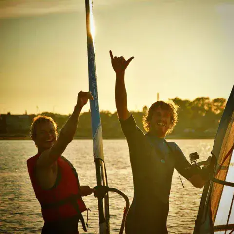 Deux windsurfeurs au coucher du soleil devant leurs voiles