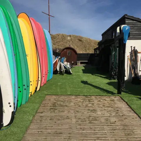 Rangée de planches de surf sur le gazon devant les cabanes du camp