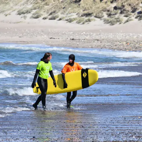 Deux élèves portant une planche de surf vers l'eau