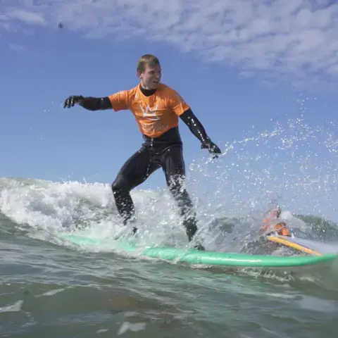 Élève de surf debout sur une planche dans une vague