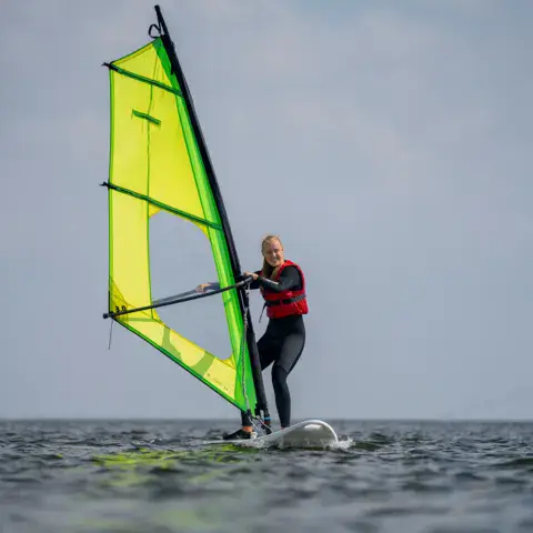 Windsurfeuse en gilet rouge sur un plan d'eau calme