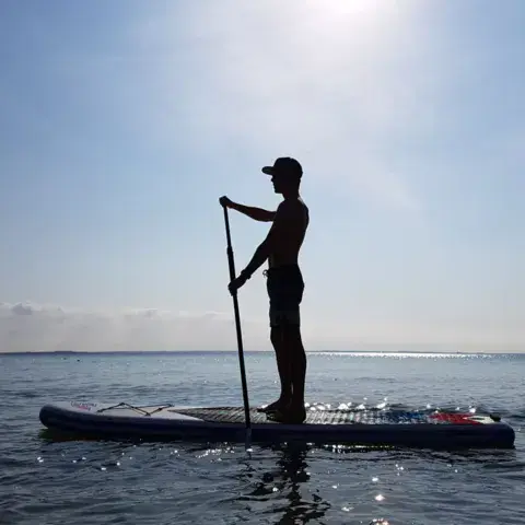 Pratiquant de paddle en contre-jour sur une eau calme