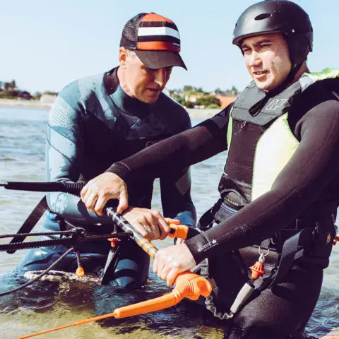 Moniteur aidant un élève à tenir la barre de contrôle dans l'eau peu profonde