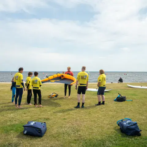Groupe en chasubles jaunes sur l'herbe au bord du fjord avant une session de kite