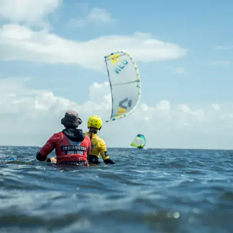 Moniteur et élève dans l'eau, face à une aile de kitesurf