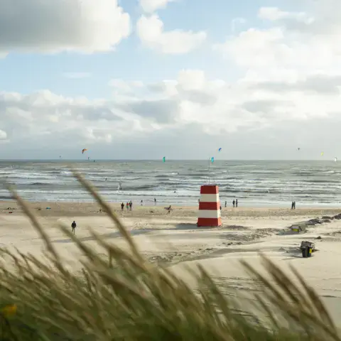 Plage de la mer du Nord avec une tour rouge et blanche et des ailes de kite au loin