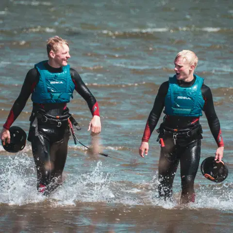 Deux moniteurs en gilets sortant de l'eau, barre de kite à la main