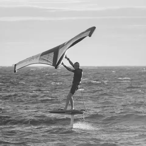 Wingfoiler en vol au-dessus de l'eau, en noir et blanc