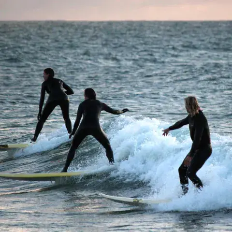 Trois surfeurs sur une vague au crépuscule