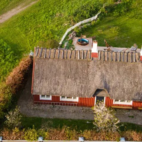 Maison à toit de chaume entourée de prairie, vue du ciel