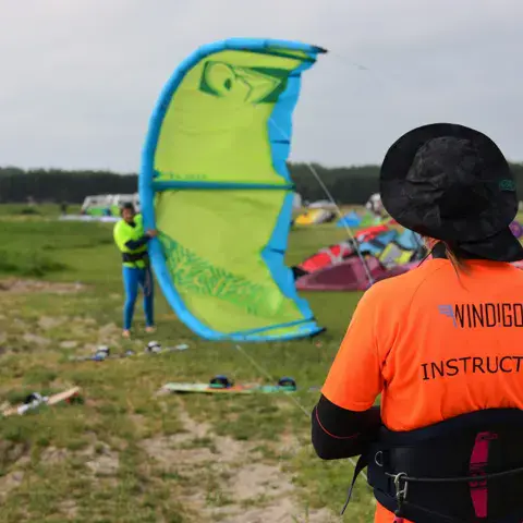 Moniteur en tenue orange sur un champ, avec un kite déployé