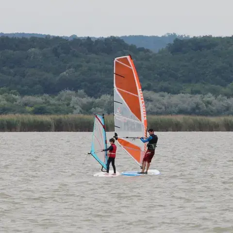 Deux planches à voile sur un lac, voiles orange et blanche
