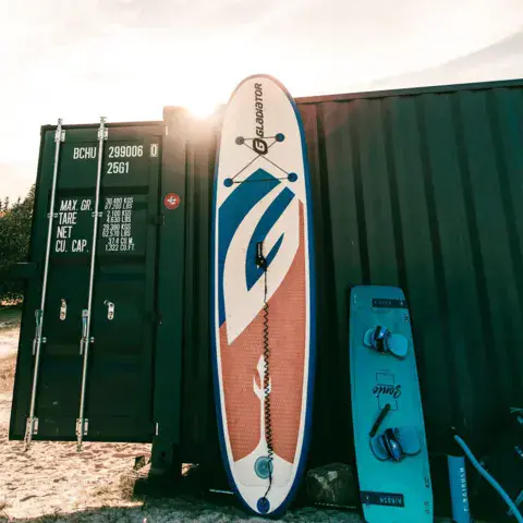 Paddle et planche de kite appuyés contre un container