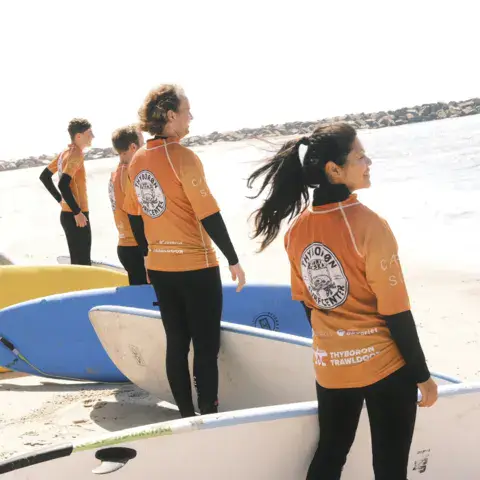 Équipe en tenue orange face à la mer, avec des planches de surf