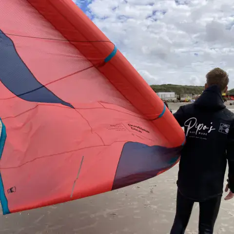 Moniteur de dos tenant une aile de kite sur la plage