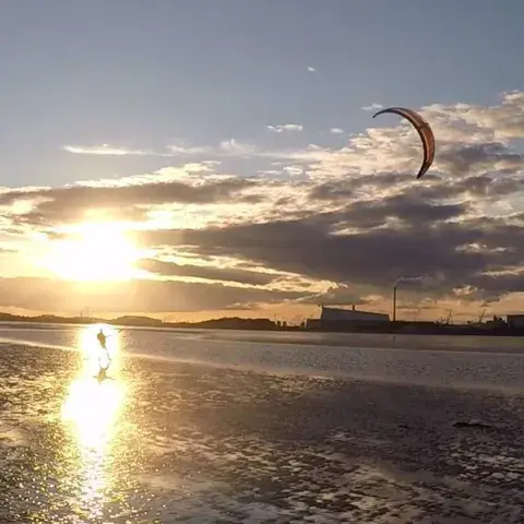 Kite dans le ciel au coucher du soleil, au-dessus d'une plage de sable mouillé