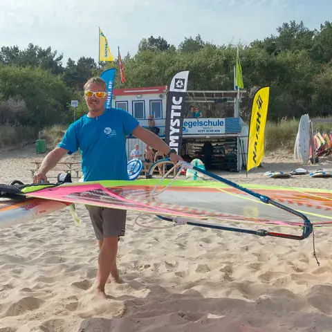 Moniteur qui porte un gréement de planche à voile sur la plage