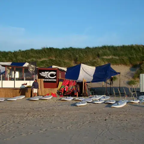 Cabane et planches de windsurf posées sur le sable