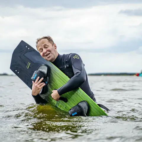 Un kitesurfeur sort de l'eau avec sa planche
