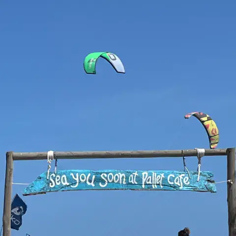 Entrée du Pallet Cafe sur la plage, avec un kite dans le ciel