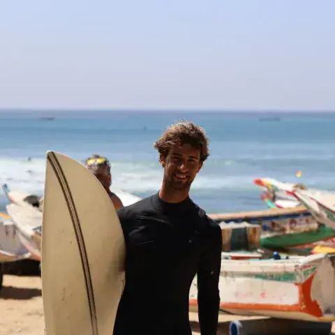 Surfeur avec sa planche devant les pirogues de la plage