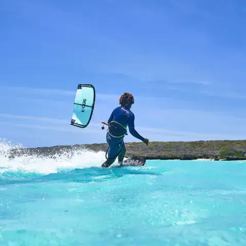 Kitesurfeur sortant de l'eau turquoise avec son aile