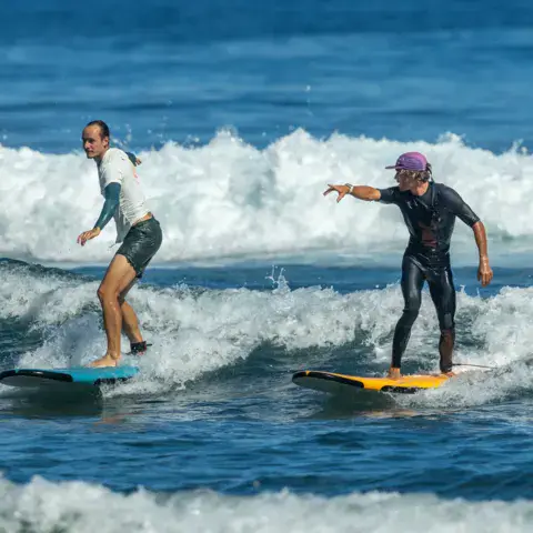 Deux élèves debout sur leurs planches dans les vagues