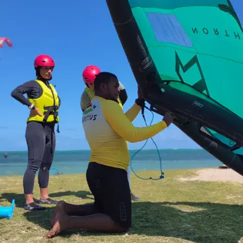 Un moniteur prépare une aile de wing foil avec une élève sur la plage