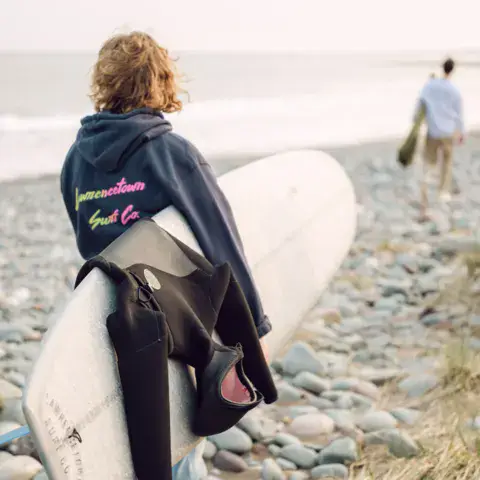 Surfeur portant sa planche sur une plage de galets