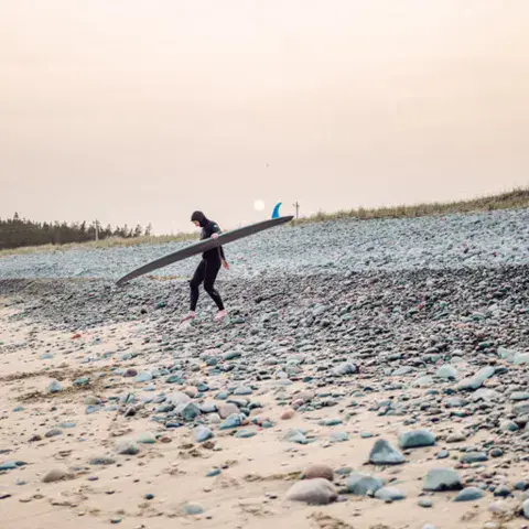 Une surfeuse traverse la plage avec sa planche sur la tête