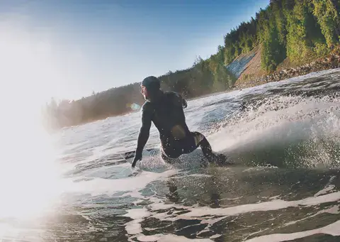 Surfeur dans une vague au bord de la côte boisée