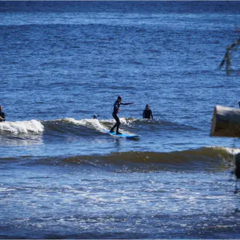 Surfeur sur une vague, entouré d'autres pratiquants à l'eau