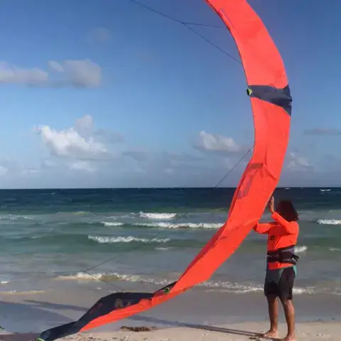 Un kiteur prépare une aile rouge sur la plage