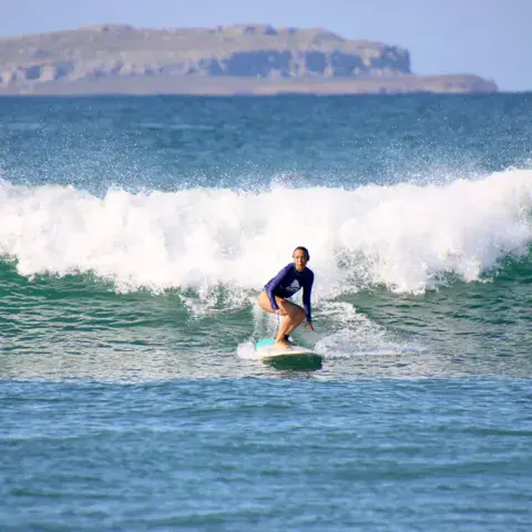 Une surfeuse sur une vague, un îlot rocheux en arrière-plan
