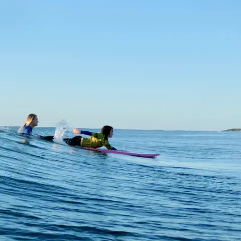 Deux surfeuses couchées sur leur planche vers une vague