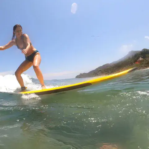Une surfeuse sur sa planche jaune, la côte boisée en arrière-plan