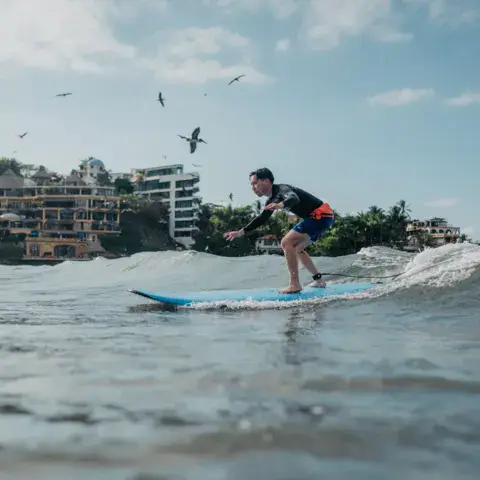 Un surfeur debout sur sa planche dans les vagues, la ville en arrière-plan