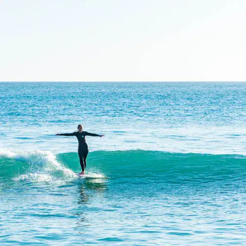 Surfeur debout sur une vague, bras écartés